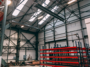 A warehouse space with red racking, overhead heating units, and roof window panels.
